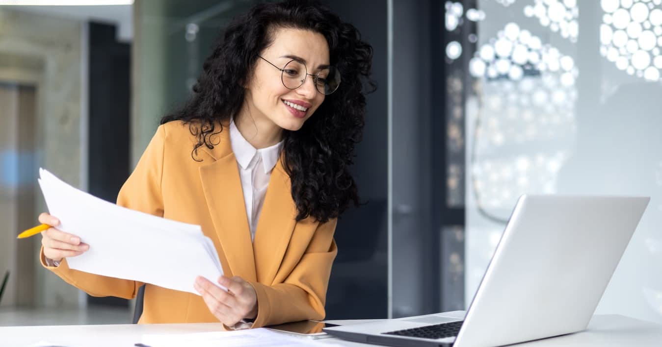 A business woman is sitting at a desk with a laptop and papers.