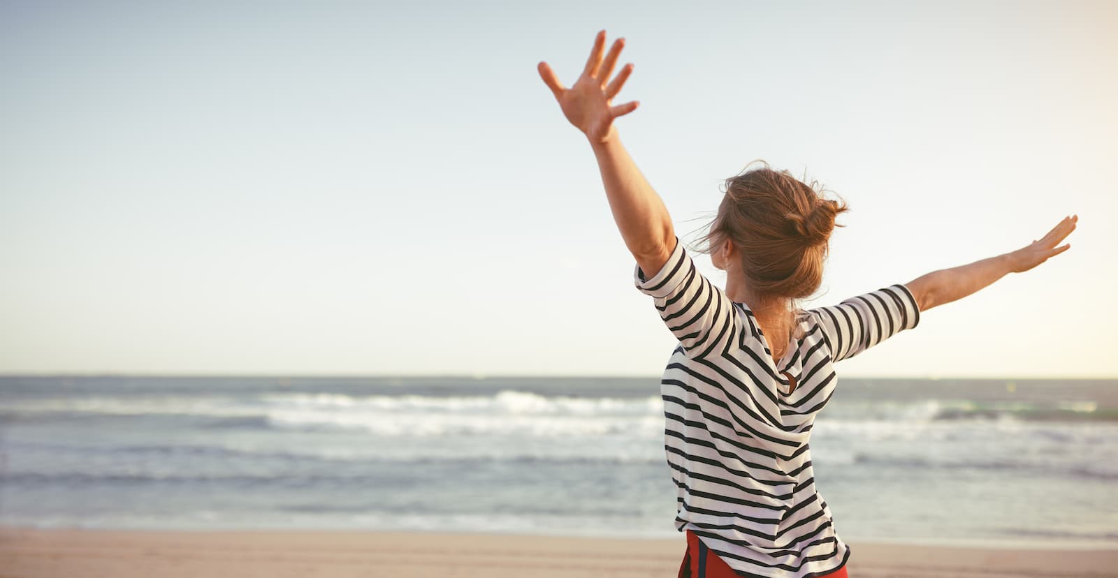 A woman standing on the beach with her arms outstretched.